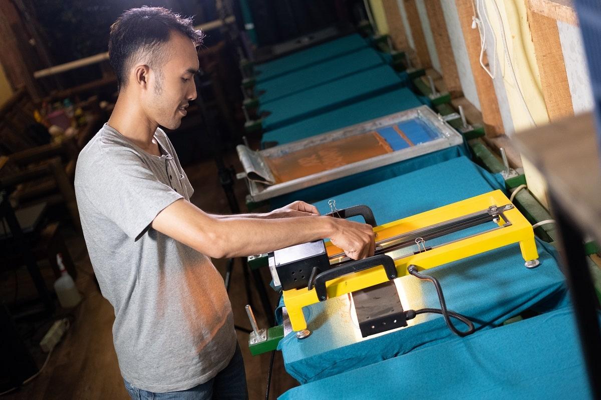 Male asian workers carefully hold the heater to dry the screen printing ink after printing the t-shirts. Differences between screen printing and dtg printing.