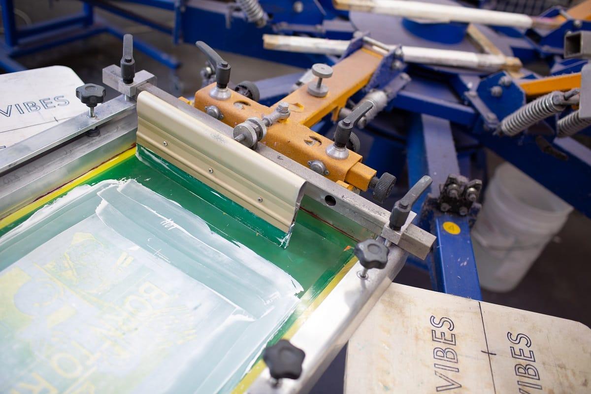 Serigraphy silk screen print process at clothes factory. Carousel frame, squeegee and plastisol color paints. What are the advantages and disadvantages of screen printing.