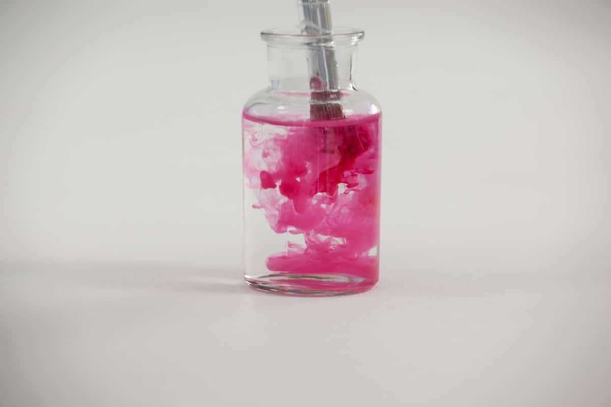 Paintbrush with pink paint dipped into a jar filled with water against white background. Things to remember while cleaning your brushes.