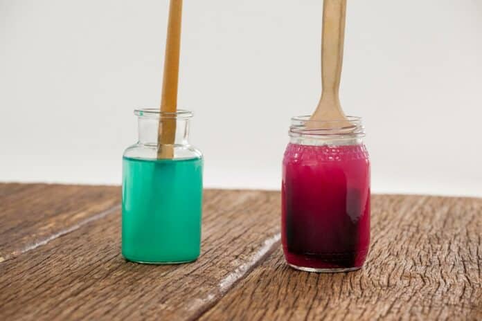Paint brushes with blue and red paint dipped into water. How To Clean Acrylic Paint Brushes Between Colors.