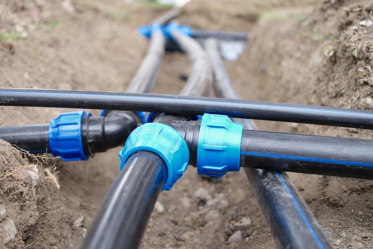 Close-up of plumbing water drainage or underground irrigation system. Elbow fittings and pvc pipes at bend in trench outdoors. Place the vents and lines.