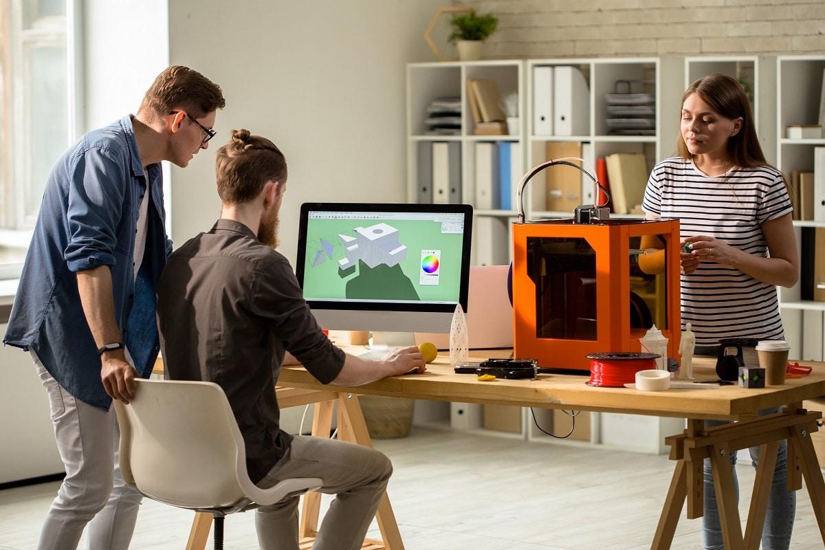 Back view portrait of young people working with 3d printer operating it via pc in modern design studio. The 3d printing process.