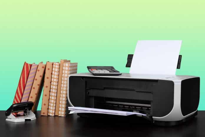 Home laser printer on desk against green background, close up. Why Laser Printer Is Better Than Inkjet.