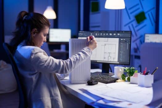 Woman architect analysing and matching blueprints for new building project sitting at desk. Graphic designer using arhitecture prototype plans working overtime in corporate office late at night. Architects use mac or pc conclusion.
