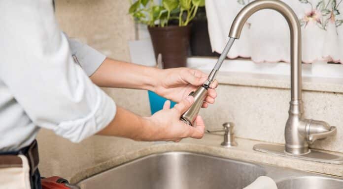 Closeup of a young man inspecting and repairing a kitchen faucet. How To Change A Kitchen Sink Faucet.