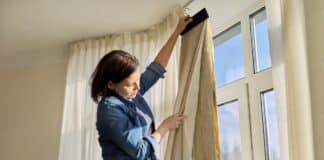 Female interior textile designer showing choosing fabrics for curtains, near panoramic window, renovation, new curtains. How To Measure For Blackout Curtains.