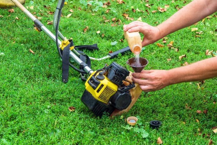 Worker pours gasoline into a trimmer or lawn mower that lies on the grass before haymaking. How much gas does a weed eater use per hour 1.