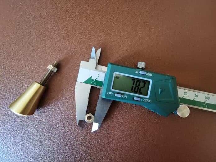 digital caliper being used to measure brass pieces