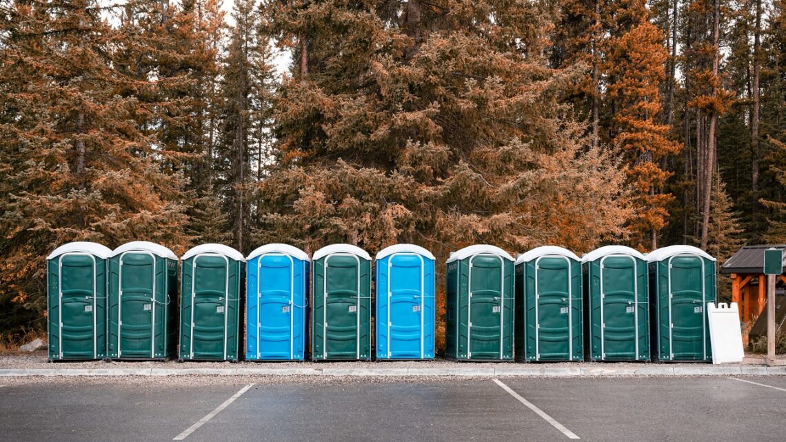 Row of green, blue portable chemical toilets in autumn forest at national park. Toilet conclusion
